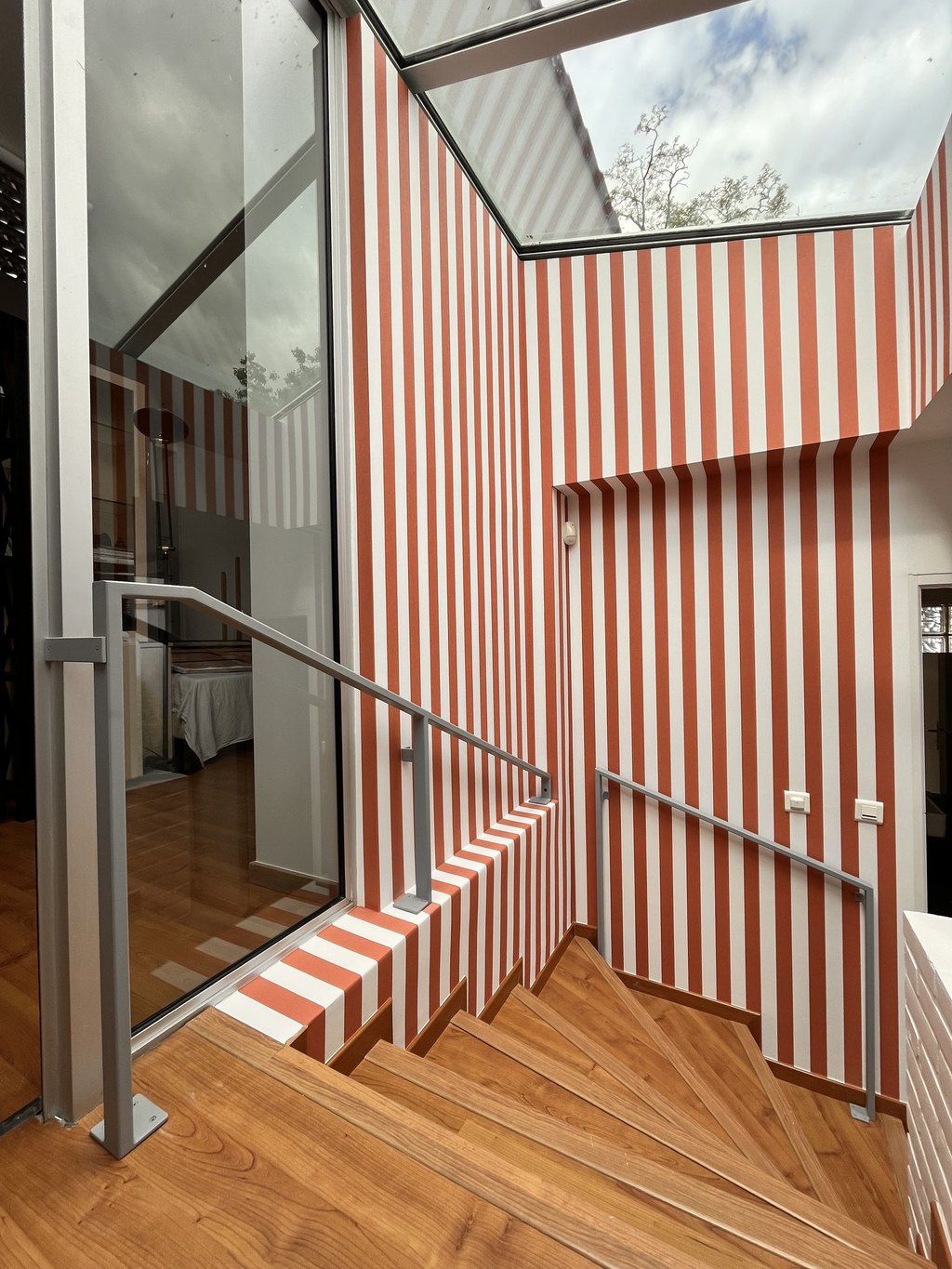 Main courante et garde-corps d’acier suivant un escalier de bois, le long d’un mur à rayures.