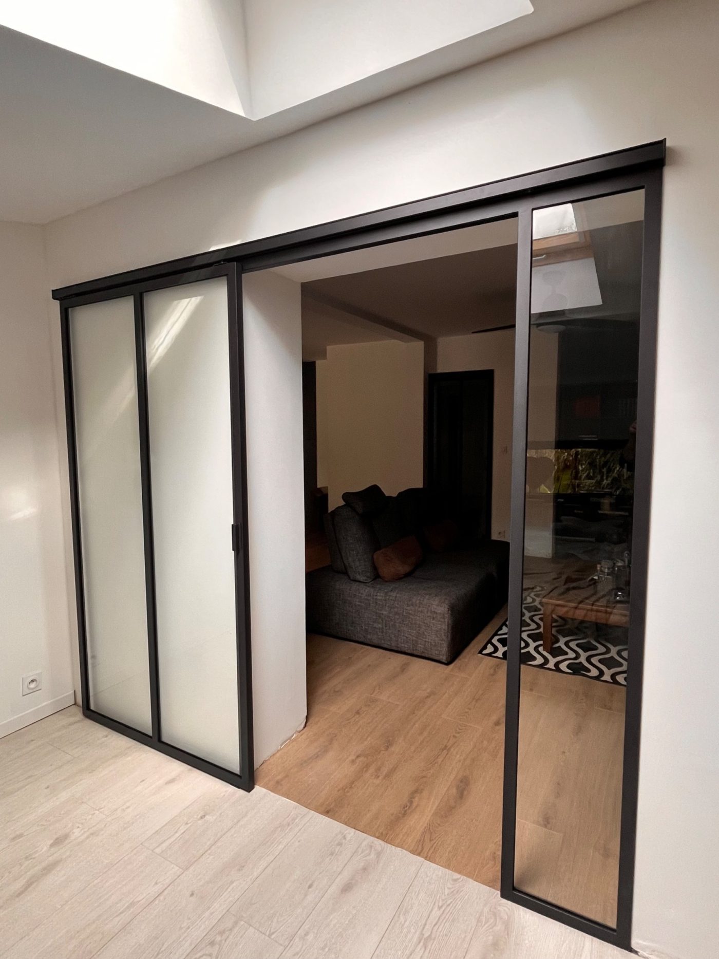 Portes coulissantes verrières en acier noir avec verre clair et verre dépoli, posées en applique entre deux pièces de vie.